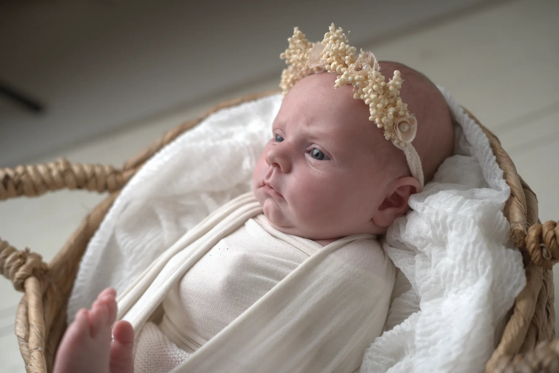 Newborn resting in a woven basket with a floral headband