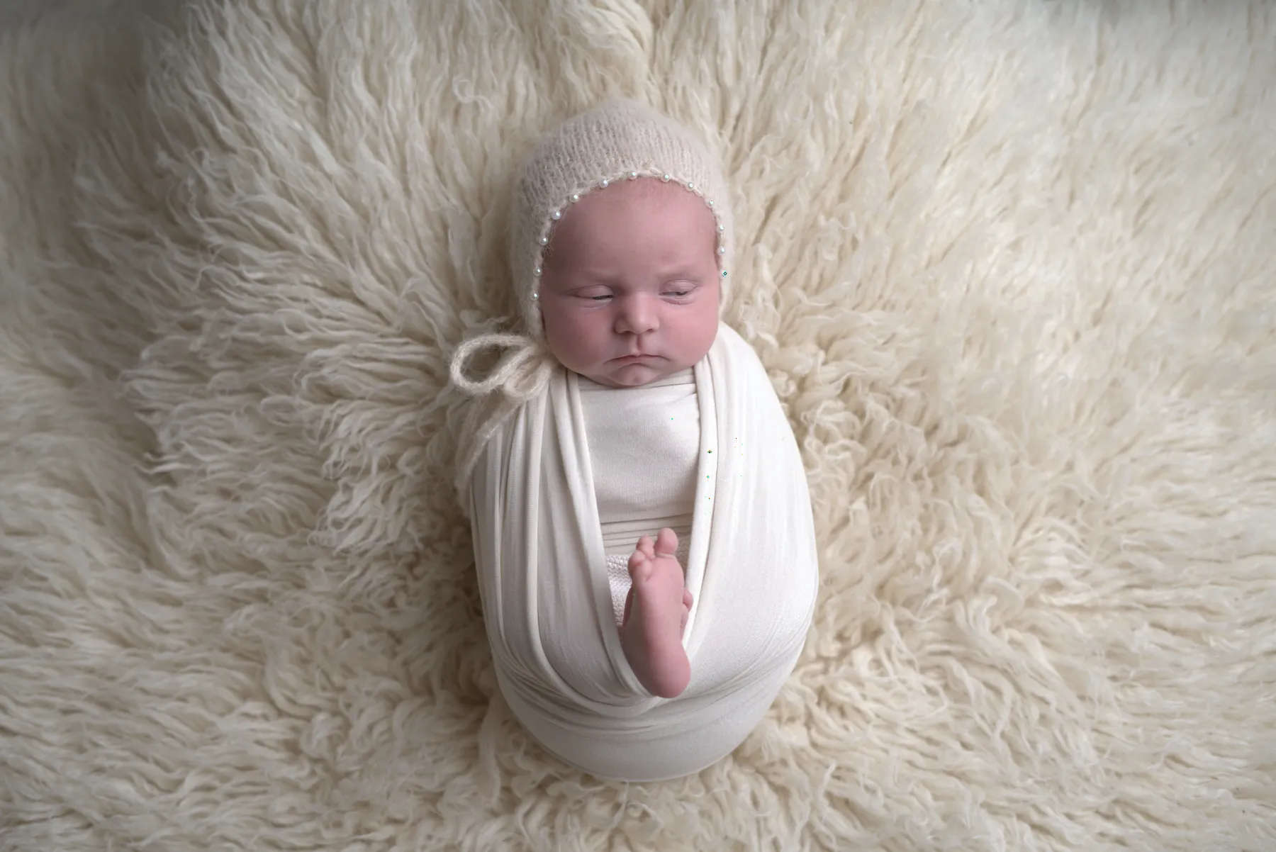 Swaddled newborn sleeping on a cream textured blanket
