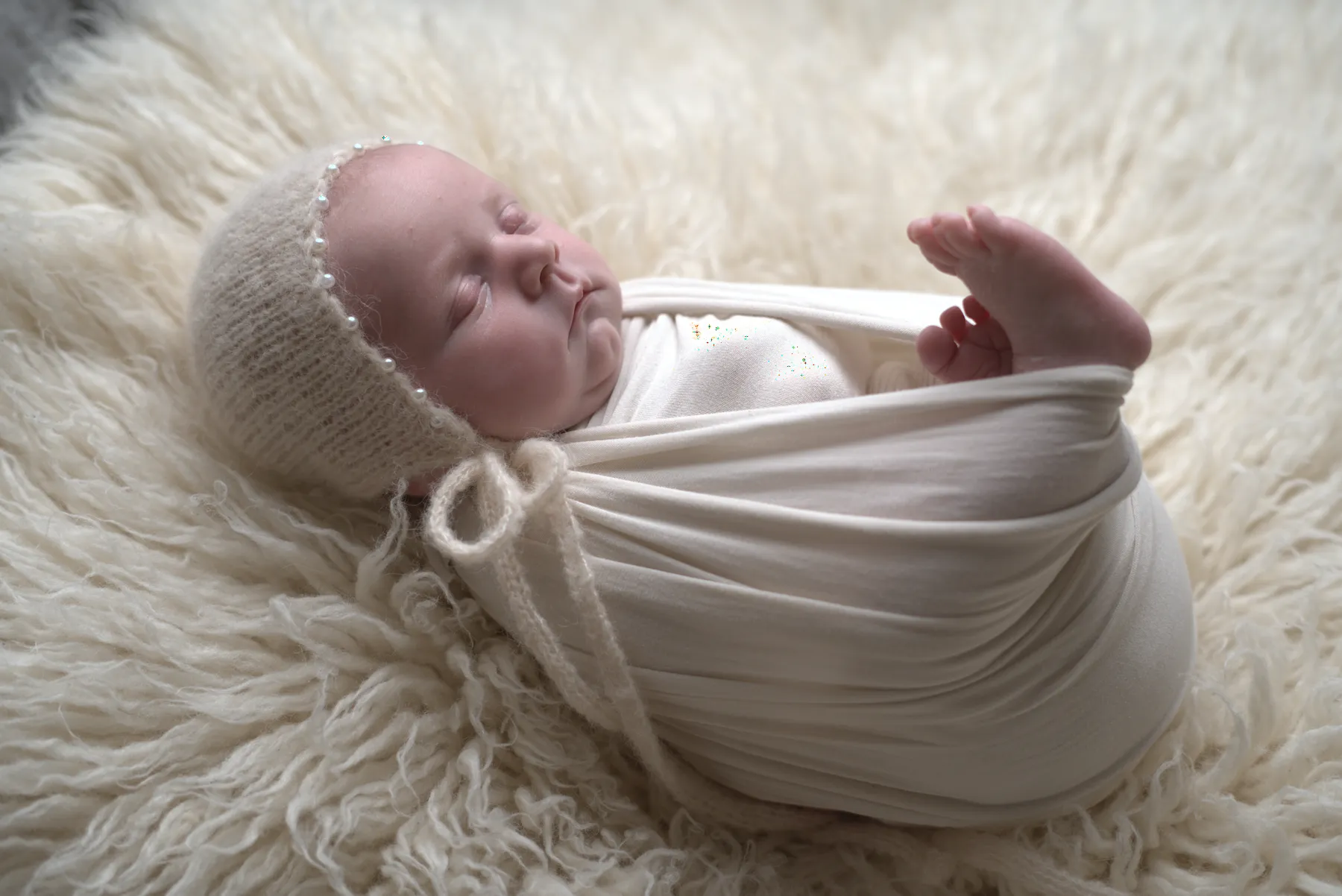 Newborn wrapped in cream on a soft textured blanket