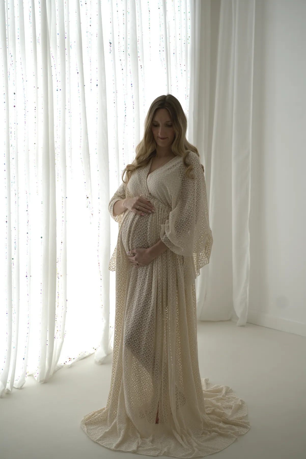 Expectant mother standing beside softly lit studio curtains