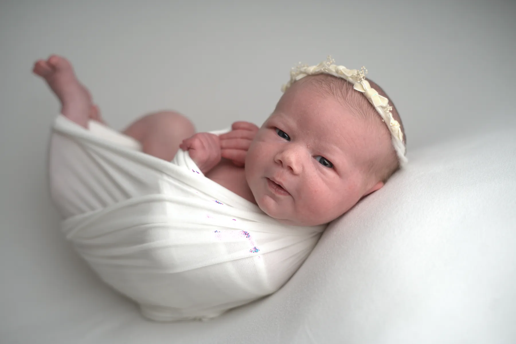 Alert newborn wrapped in cream with a floral headband