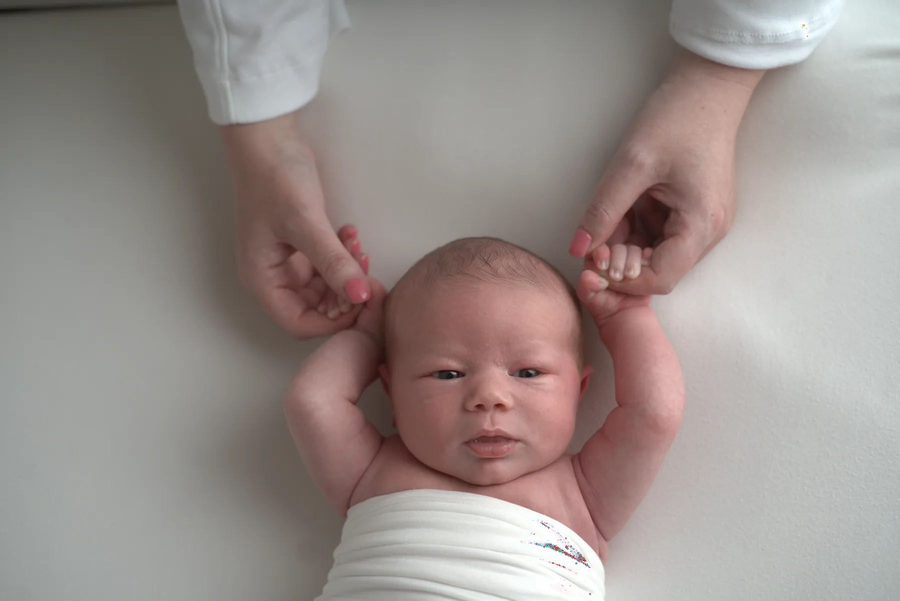 Awake newborn reaching up from a cream wrap