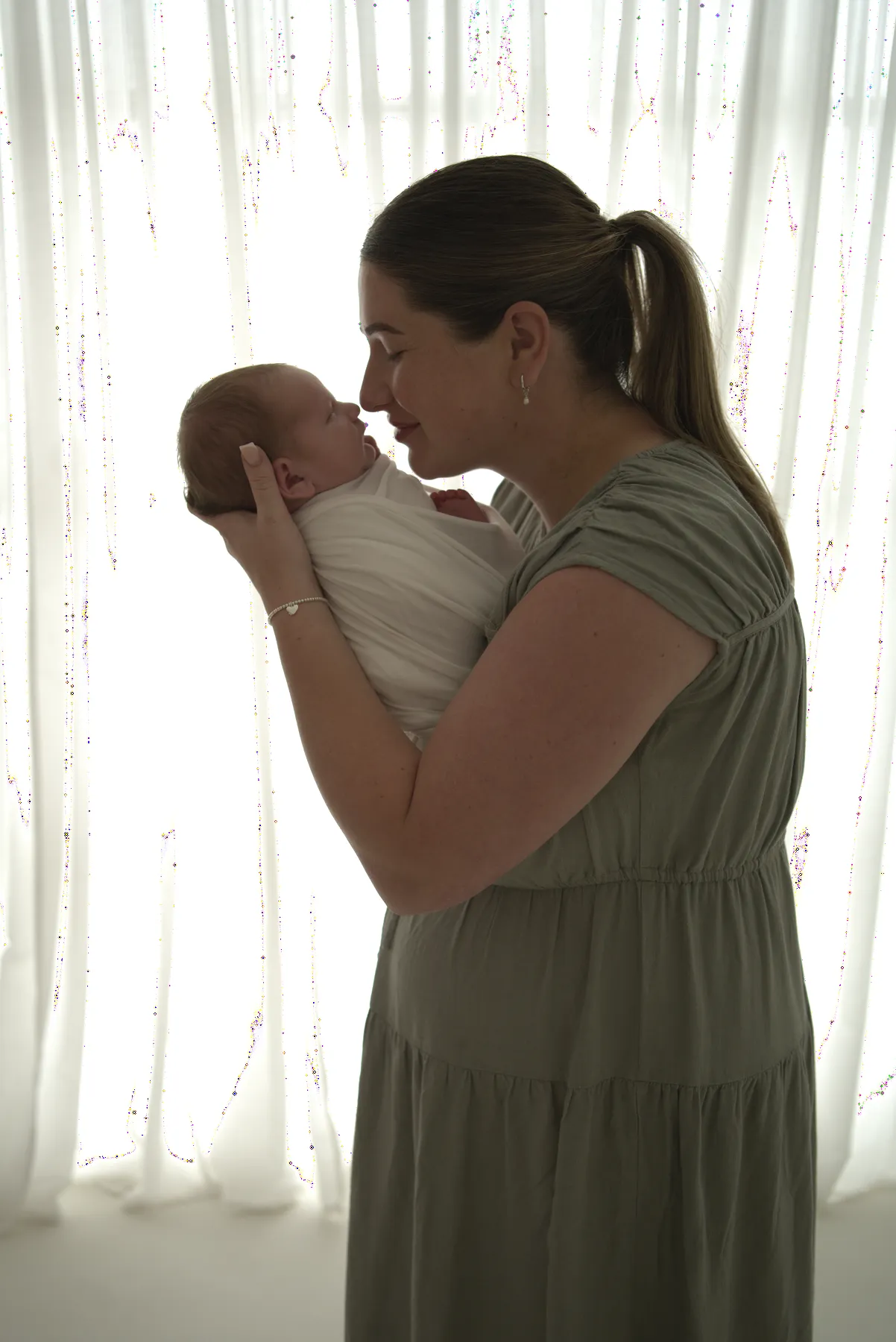 Mother holding a wrapped newborn beside a studio window
