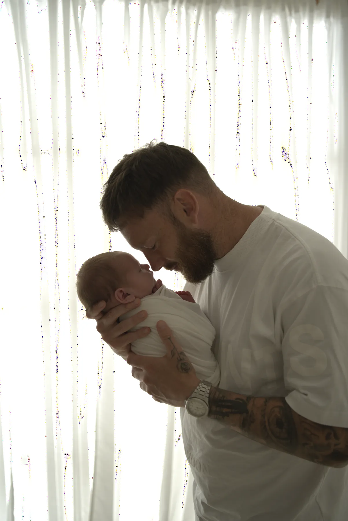 Father holding a wrapped newborn beside a studio window