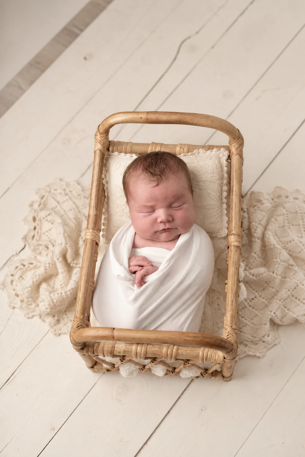 Wrapped newborn sleeping in a woven basket on a soft cream blanket