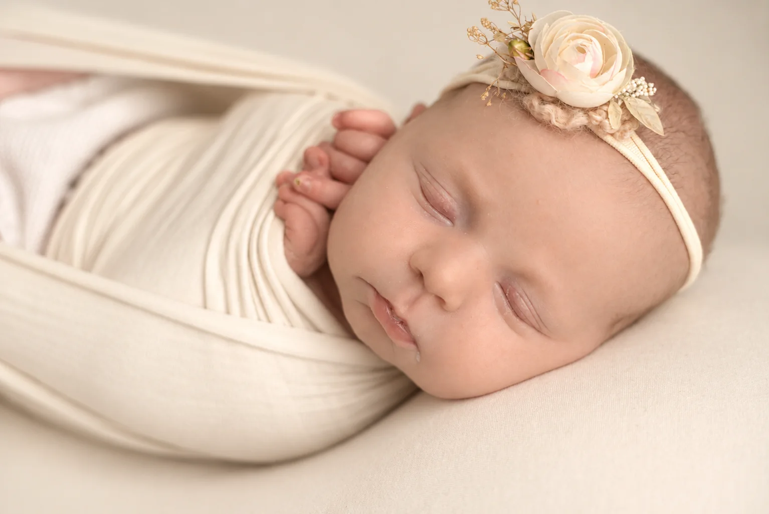 Sleeping newborn wrapped in cream with a delicate floral headband