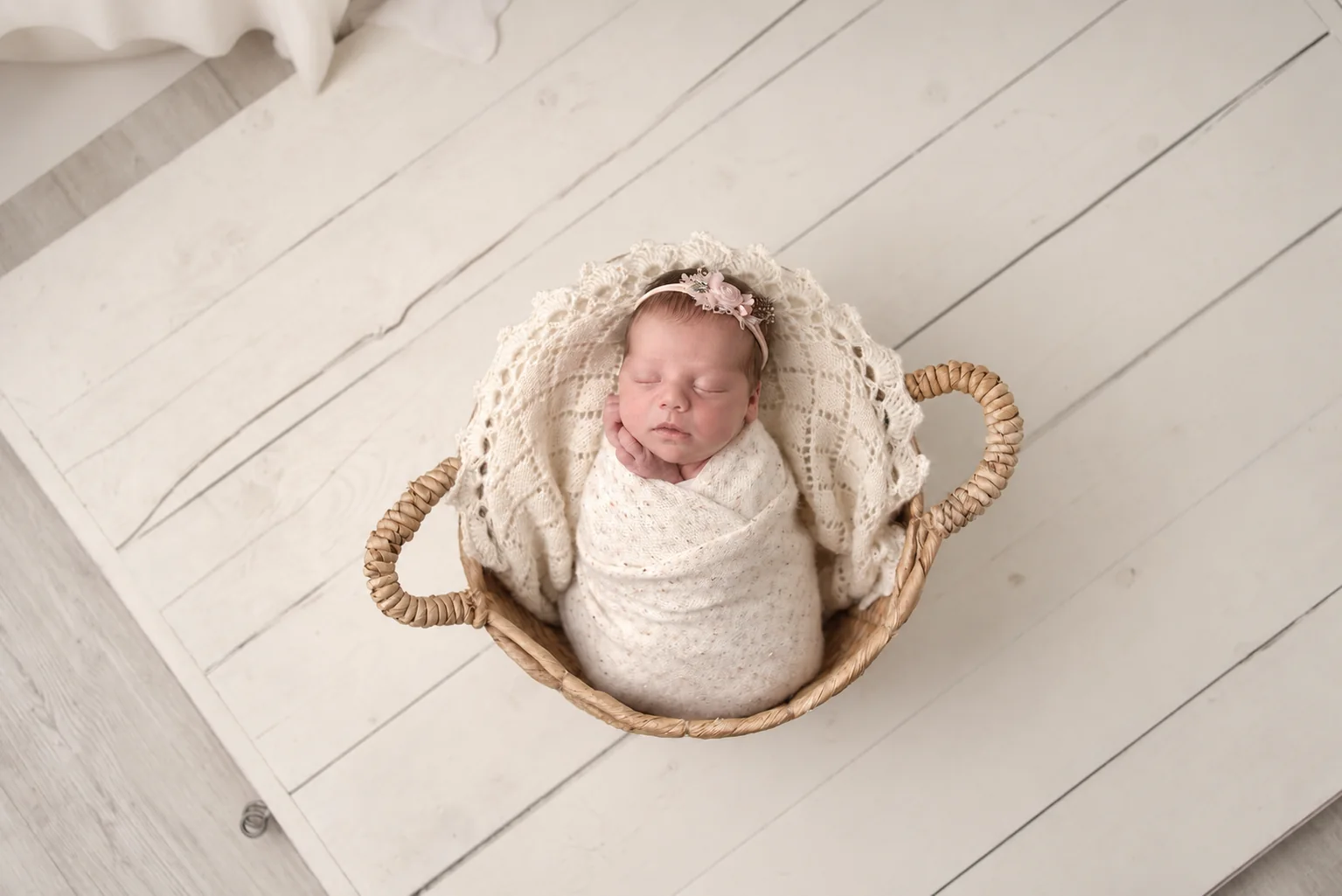 Wrapped newborn sleeping in a round woven basket with a floral headband