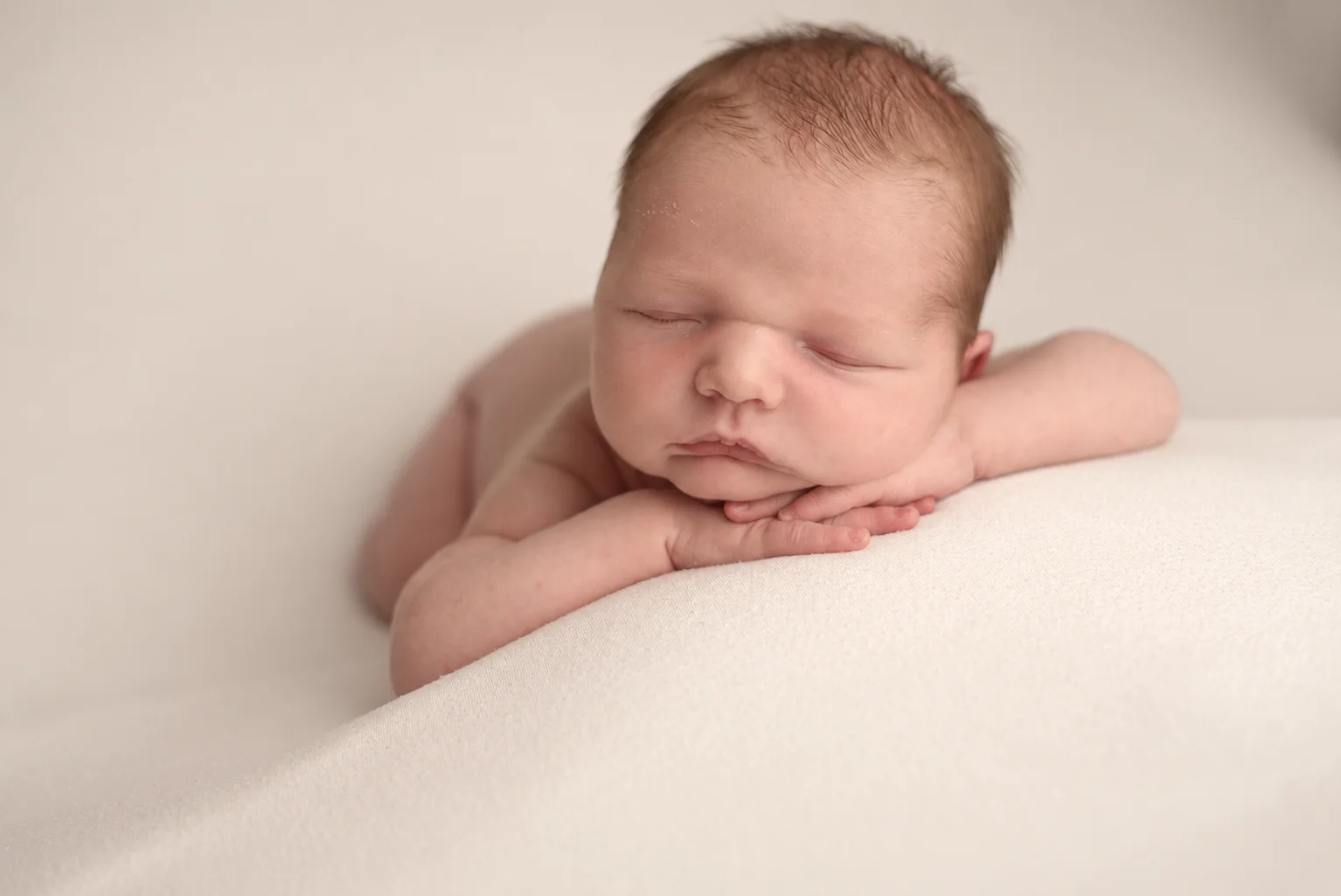 Newborn baby resting gently with their chin on folded hands